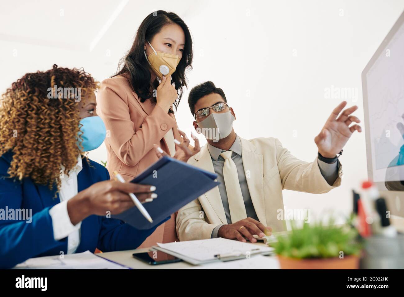 Business team in protective masks looking at chart on computer screen