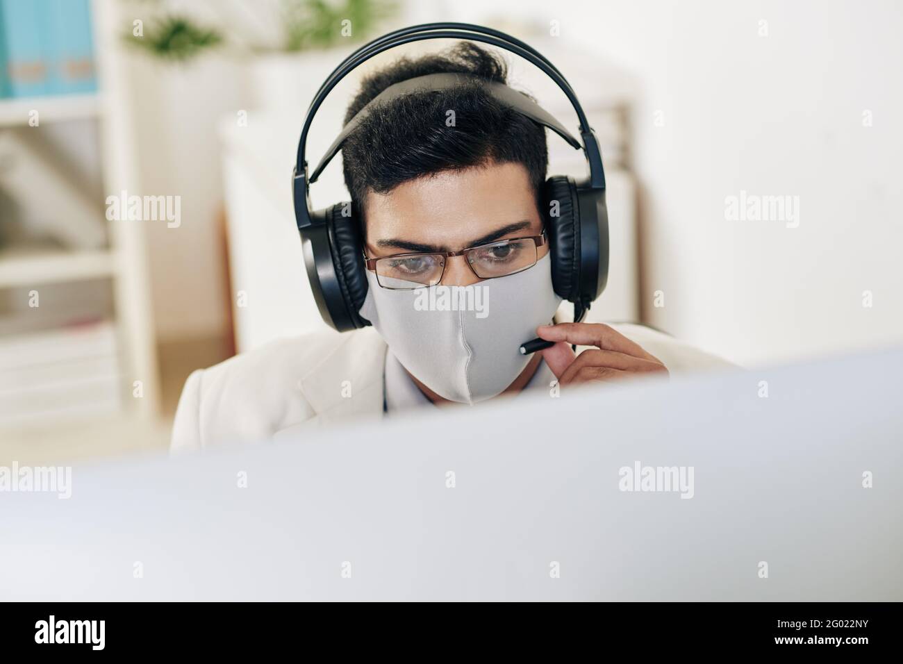 Serious technical support operator in medical mask and headphones answering phone call of customer Stock Photo