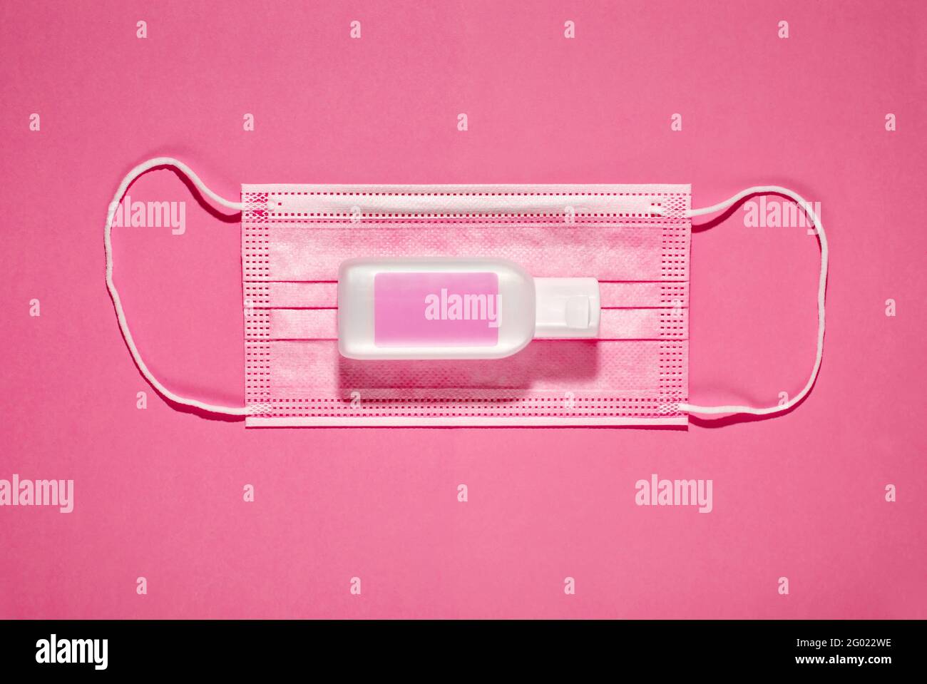 From above of clean protective pink face mask with bottle of hand sanitizer gel composed on pink background Stock Photo