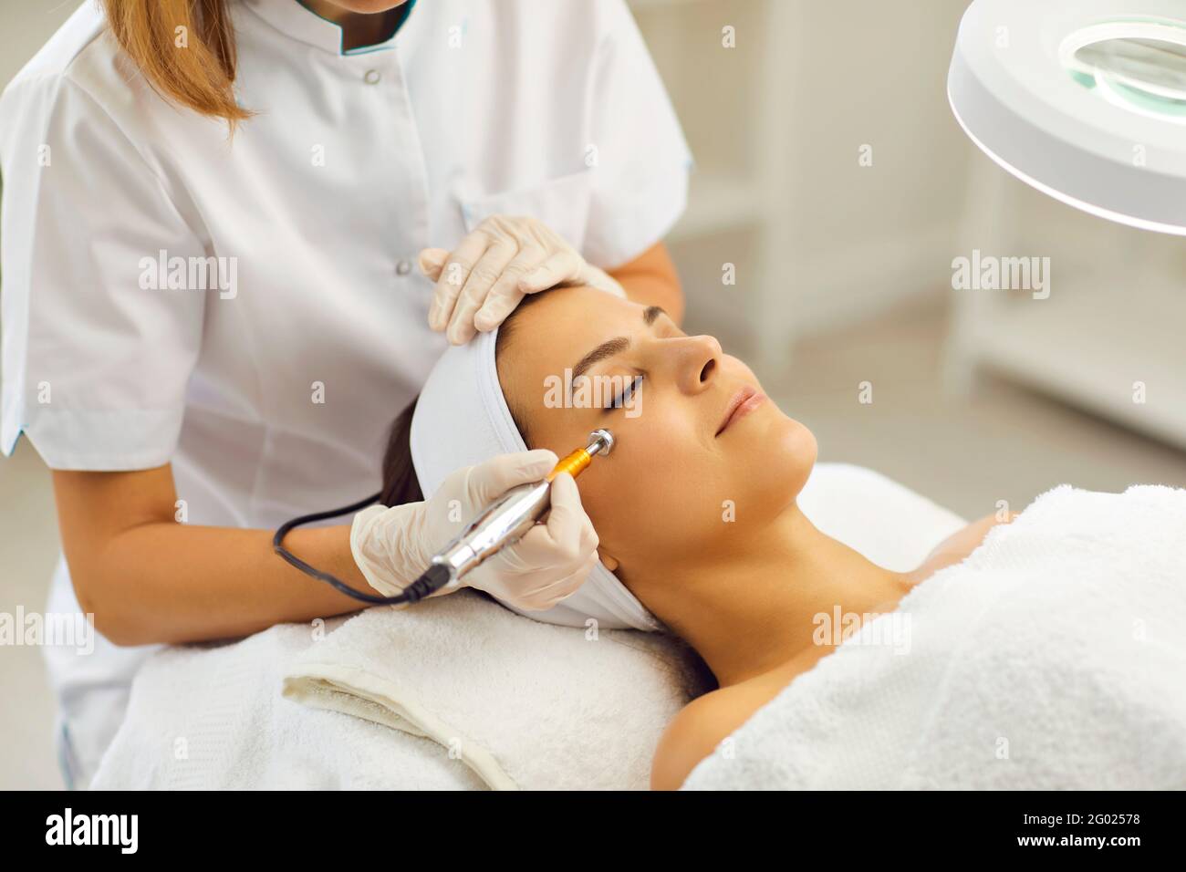 Beautician using electric mesotherapy device to decrease wrinkles on customer's face Stock Photo