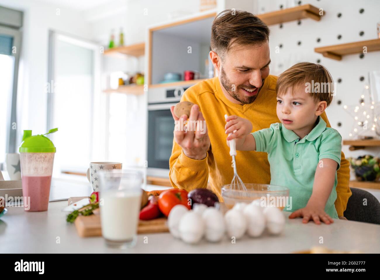 Happy single father with a toddler boy having fun and preparing healthy food in kitchen at home. Stock Photo