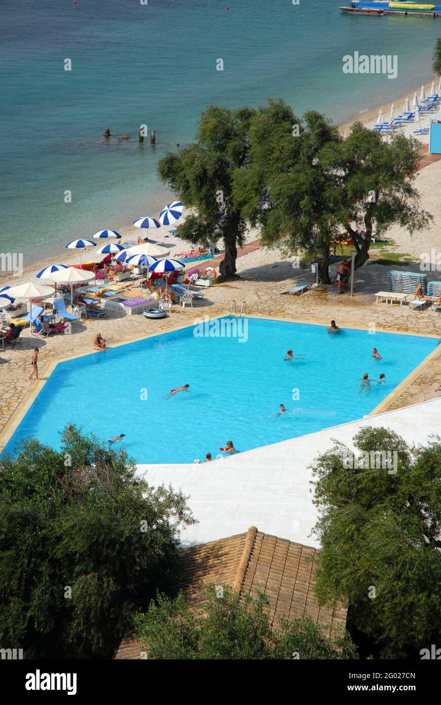 Holidaymakers enjoying the pool and other facilities at the Nissaki Beach Hotel, Corfu, Greece and the Mediterranean sea beyond Stock Photo
