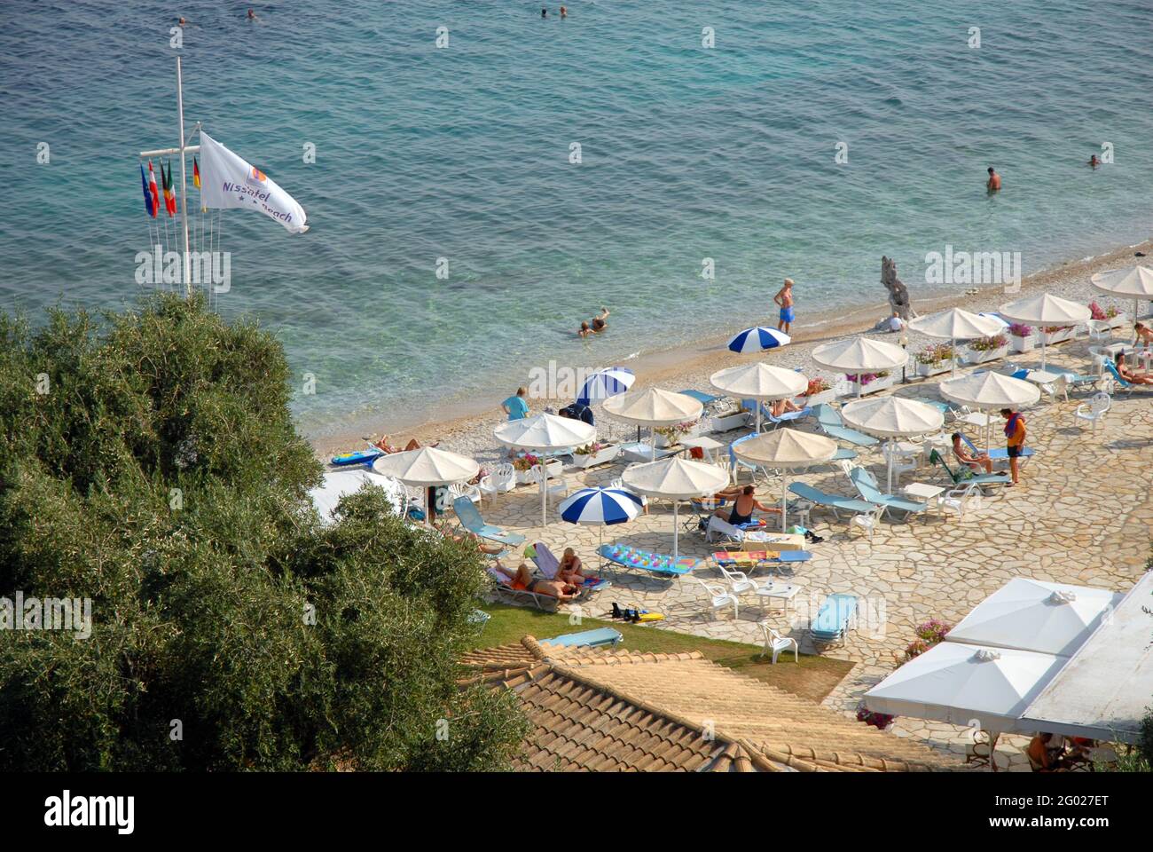 People enjoying the hotel paved area and the adjoining beach at the Nissaki Beach hotel, Corfu, Greece Stock Photo
