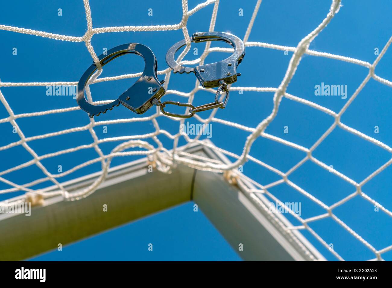 Scam with soccer or football gambling corruption. Handcuffs hanging on the net of a football goals Stock Photo