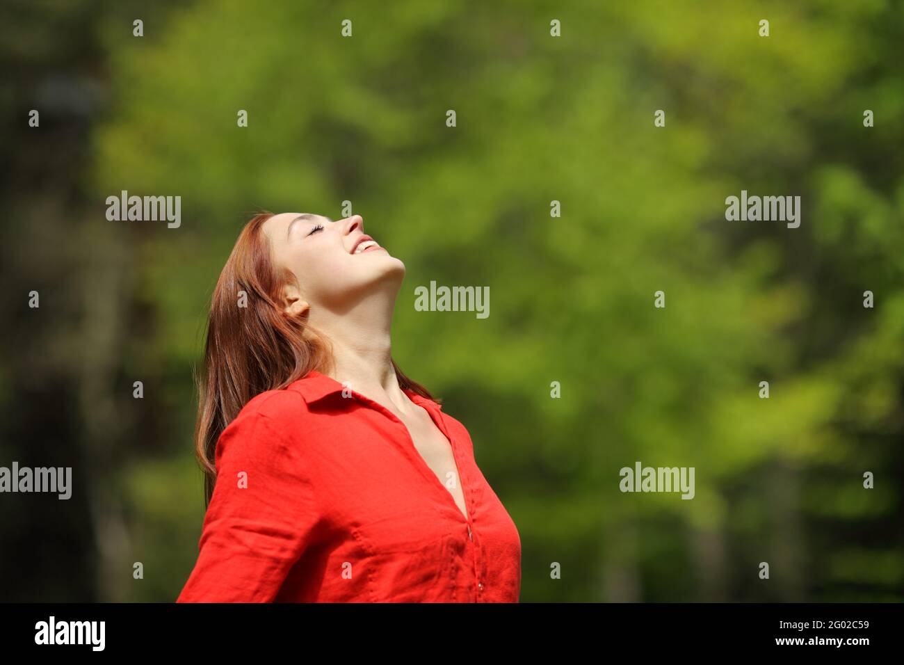 Happy woman in red breathing fresh air smiling in a forest or park ...
