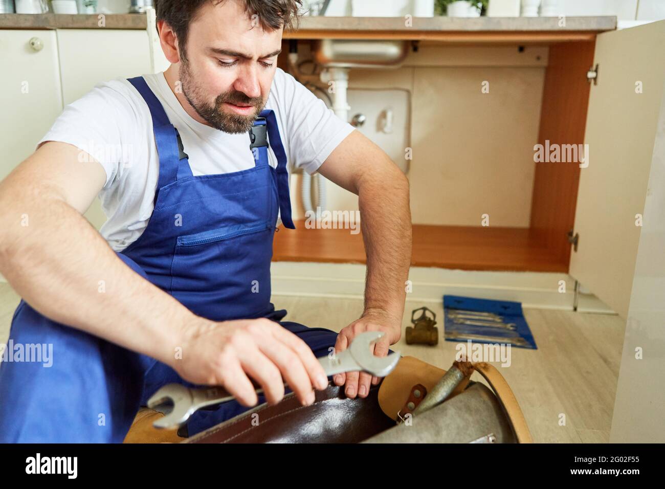 Do-it-yourselfer looks uncertainly at his tools to repair the defective kitchen sink Stock Photo