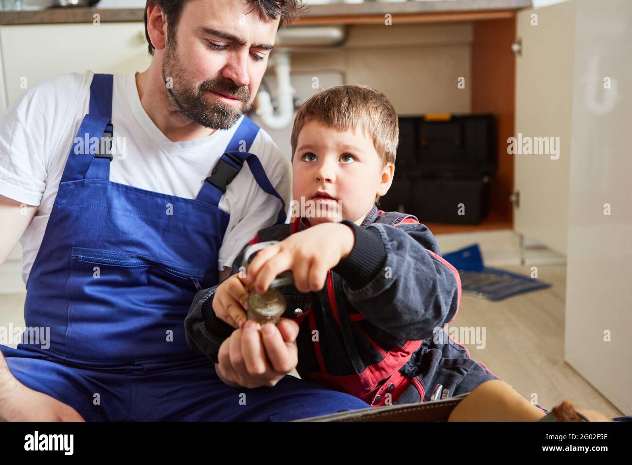 Boy with broken shutoff valve in the kitchen sink helps his father