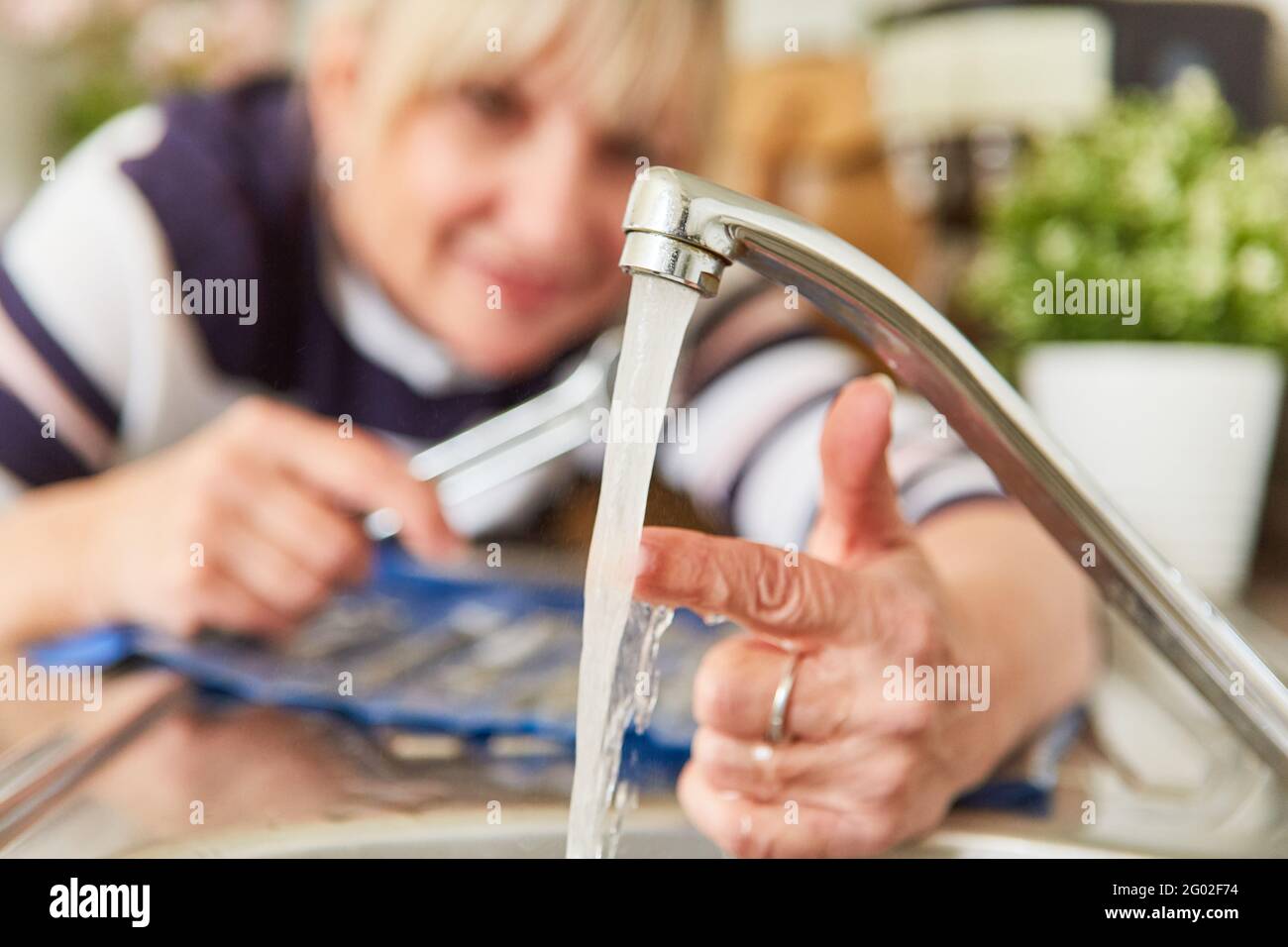 Woman working as a handyman checks the temperature of the hot water on the tap of the sink Stock Photo