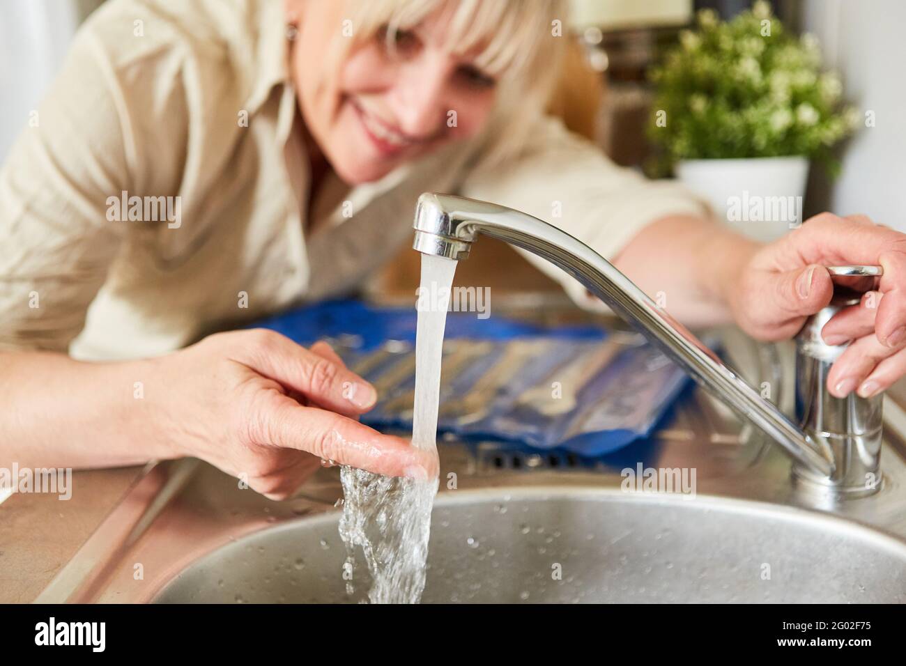 Handyman woman checks mixer tap for hot water on the sink in the kitchen Stock Photo