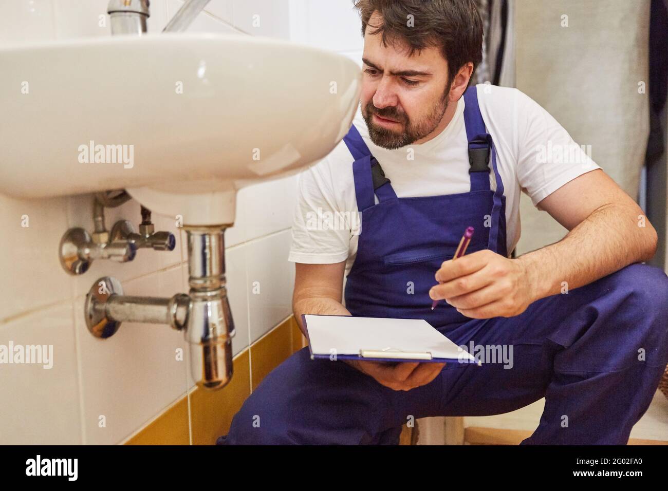 Plumber with checklist on clipboard after repairing siphon on sink Stock Photo