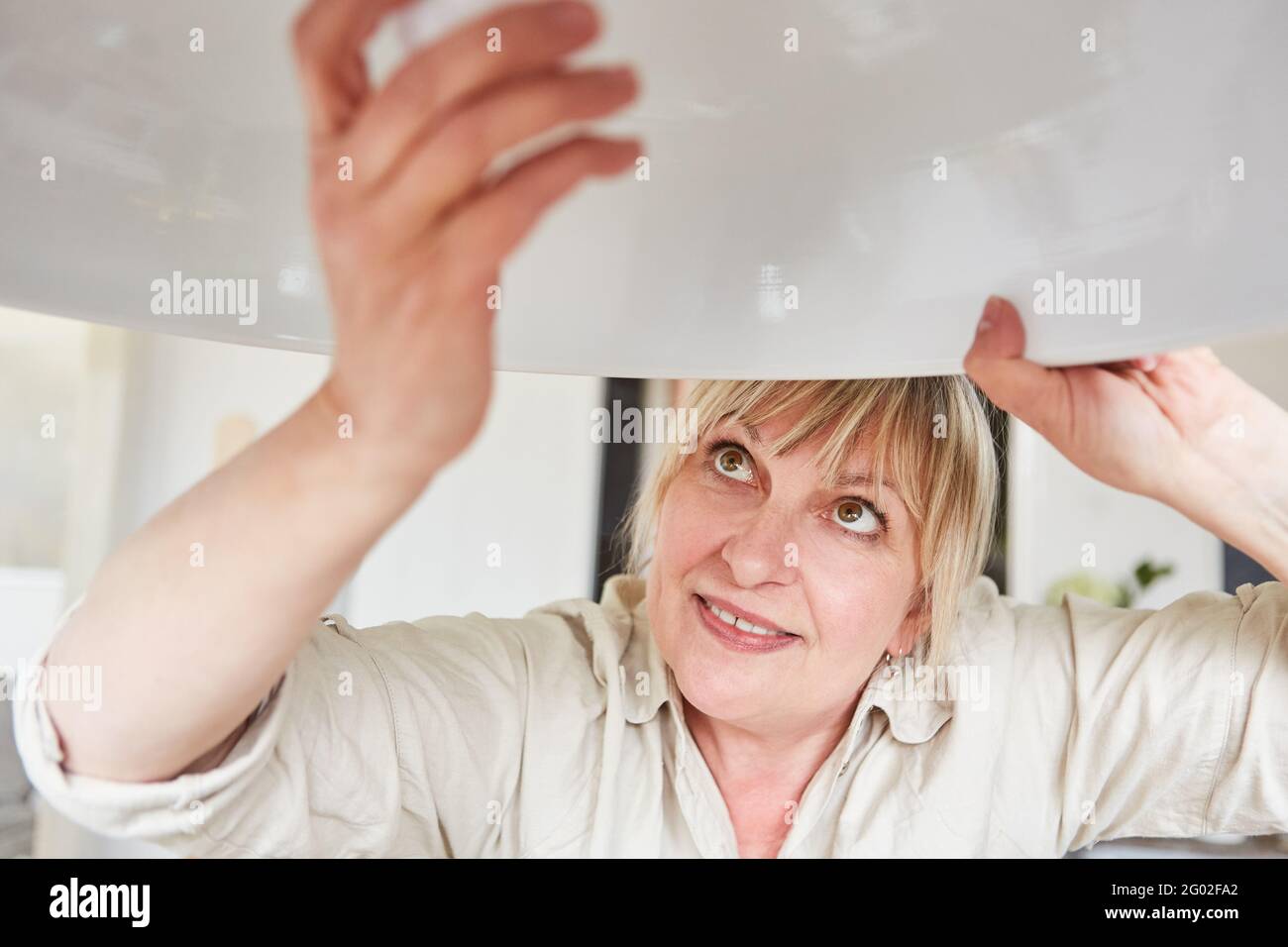 Handyman woman changes LED lightbulb on energy-saving lamp at home Stock Photo