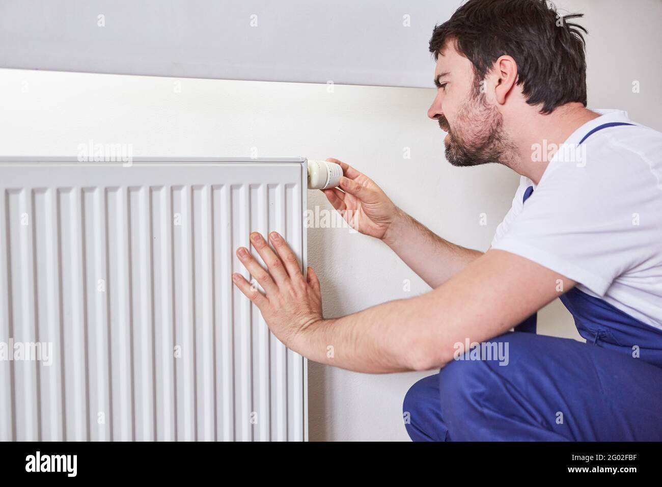 Installer or do-it-yourselfer adjusts the thermostat on the radiator of a heating system Stock Photo
