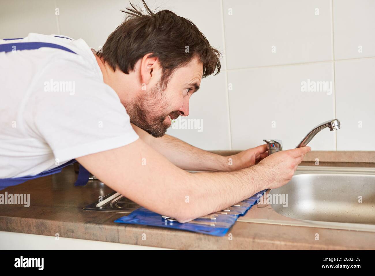 Plumber or handyman plumber repairs faucet on the sink in the kitchen Stock Photo