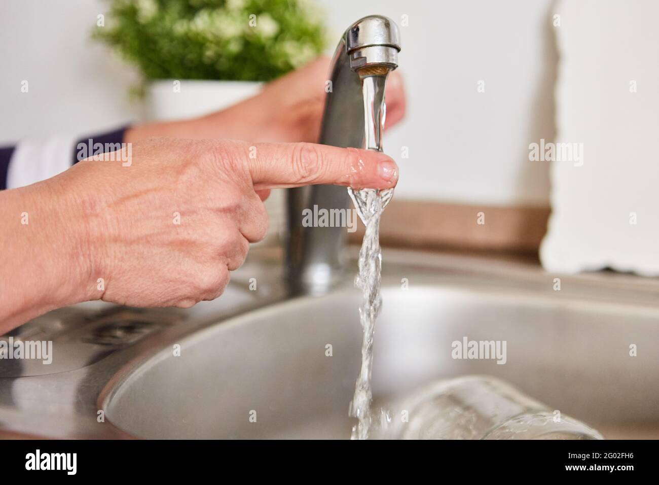Finger under the running water on the tap of the sink checks the hot water Stock Photo