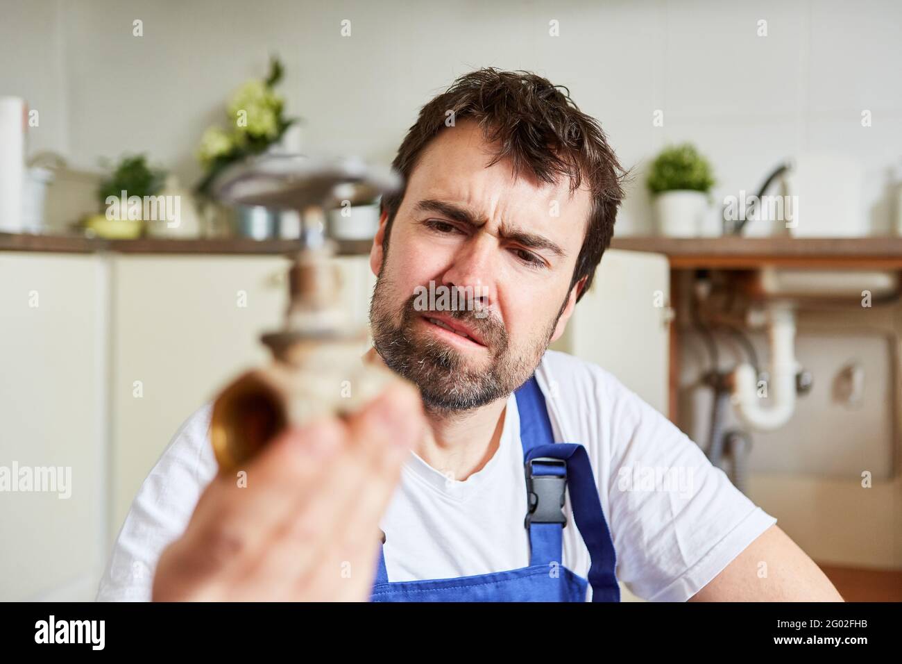 Do-it-yourselfer looks uncertainly at a defective shut-off valve for drain repair Stock Photo