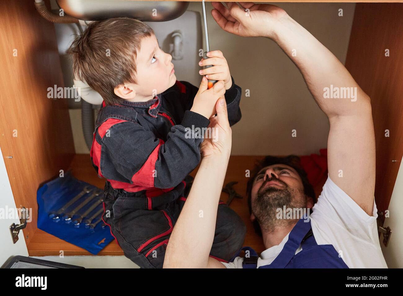 Boy helps his father as a do-it-yourselfer to repair a broken kitchen sink Stock Photo