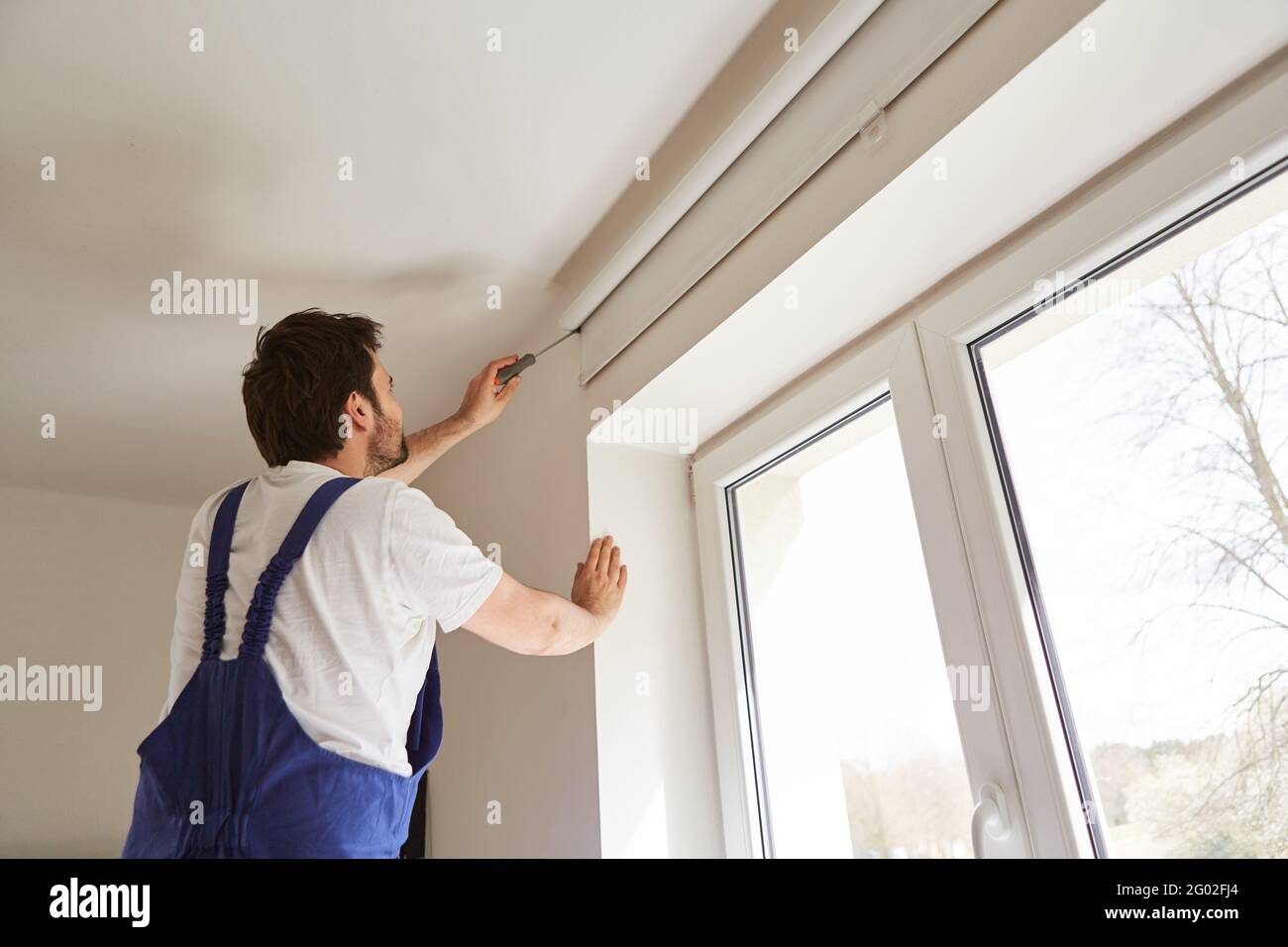 Craftsman or do-it-yourselfer installing a blind on the window of an apartment Stock Photo