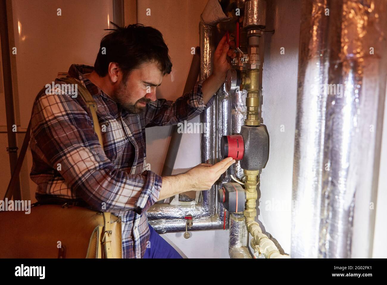 The heating installer checks the circulation pump of the heating system in the basement during maintenance Stock Photo