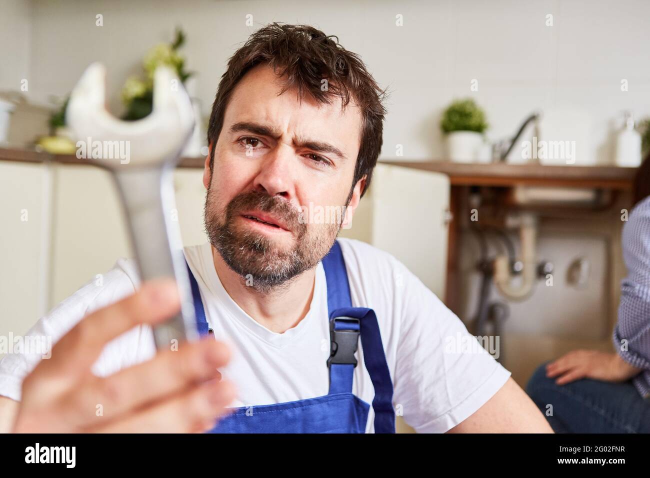 Handyman with large open-end wrench to repair the kitchen sink looks uncertain Stock Photo