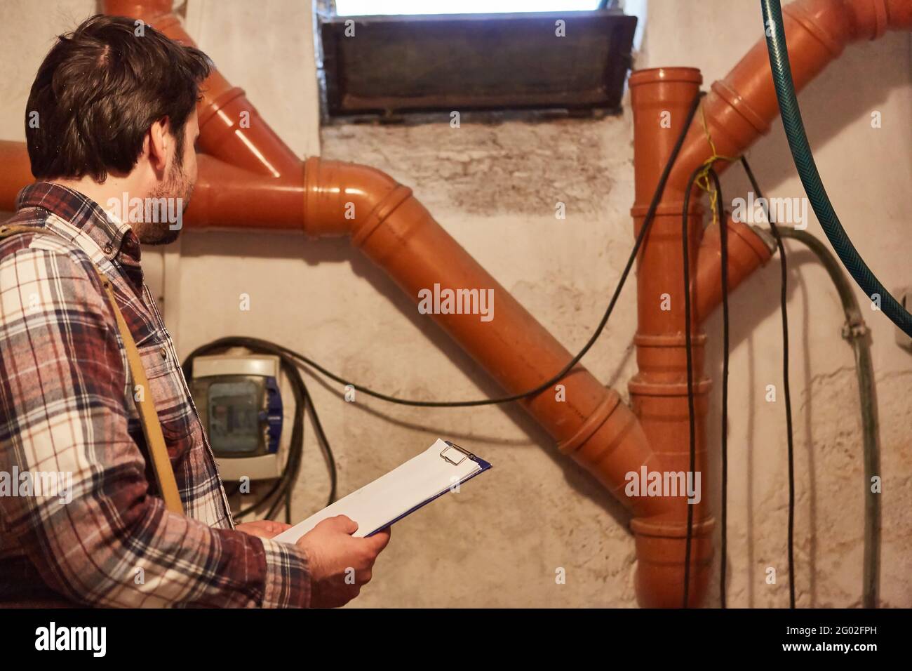 Do-it-yourselfer or craftsman checks pipes and cables in the basement with a checklist Stock Photo