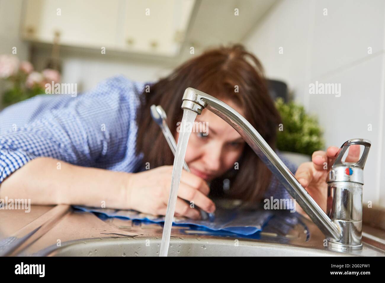 Young woman as a do-it-yourselfer installing the kitchen faucet on the sink Stock Photo