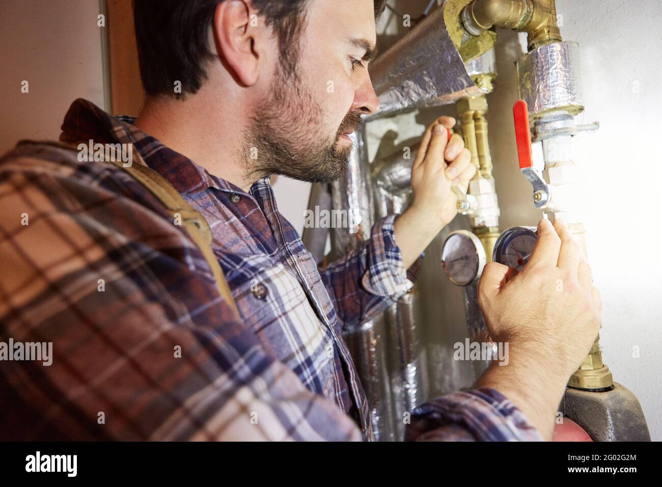 The heating installer checks the valves and water pipes on the heating system in the basement Stock Photo