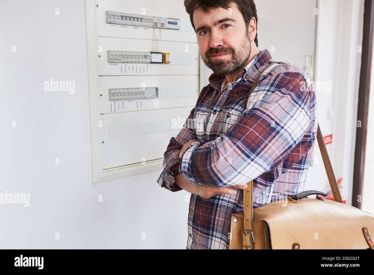 Electrician with folded arms in front of the fuse box of an apartment Stock Photo
