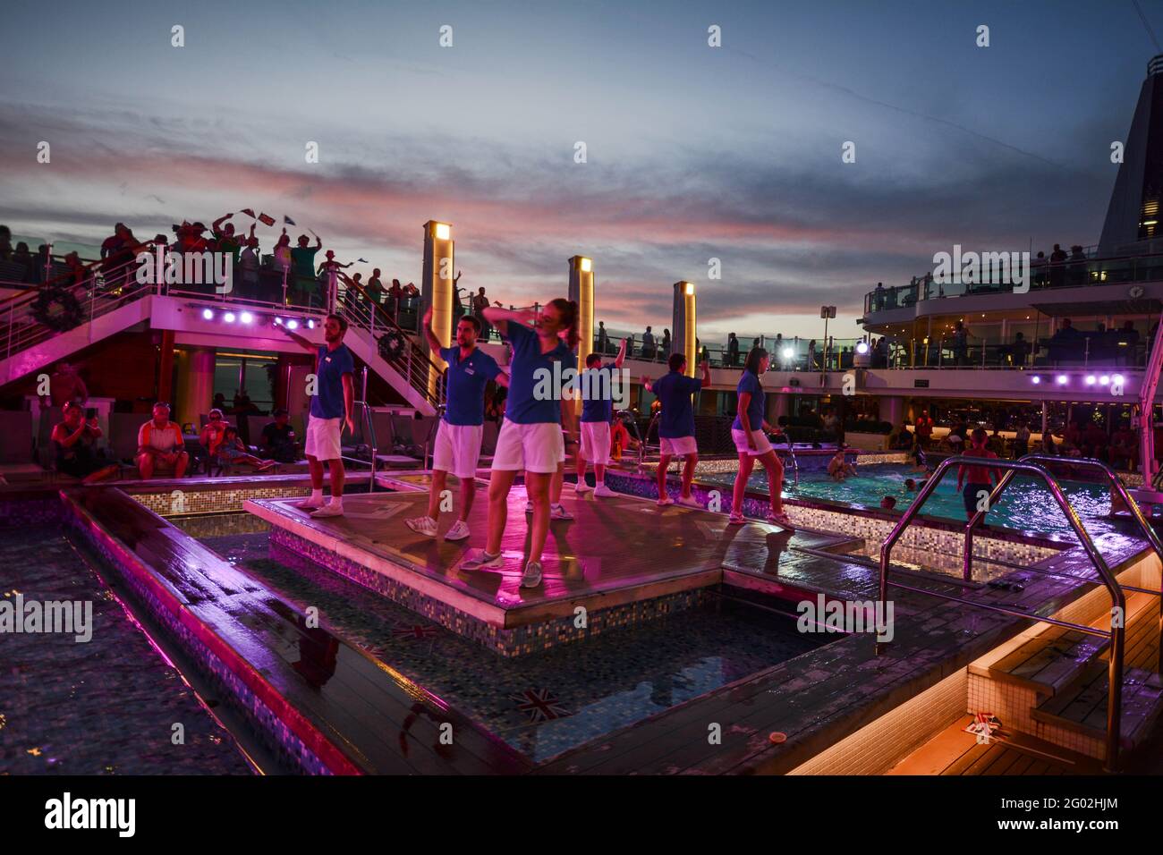Dancers on Cruise ships Azura and Britannia twilight sky pink singing dancing on a stage in shorts swimming pool entertainers entertainment pool water Stock Photo