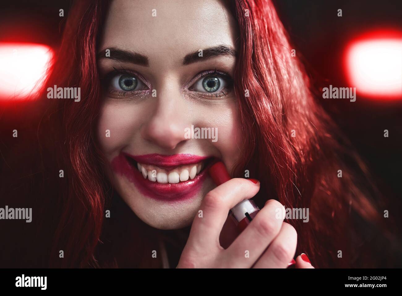 Portrait of crazy-looking teen girl with red hair she is smearing red lipstick on her face, horror concept. halloween time. Fear and nightmare Stock Photo