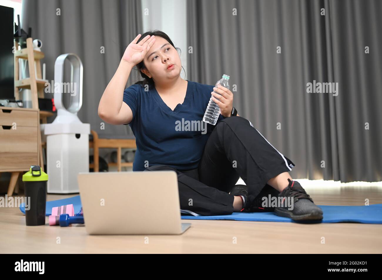 Tired young obese woman sitting and resting after doing fitness exercises at home. Stock Photo