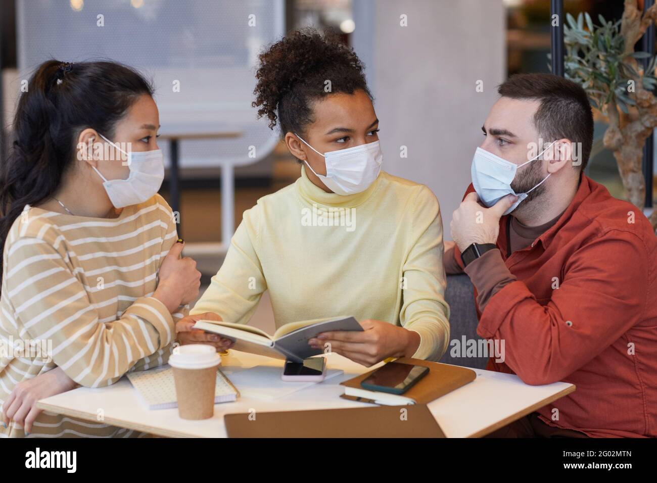 Diverse group of people wearing masks while working at table in cafe ...
