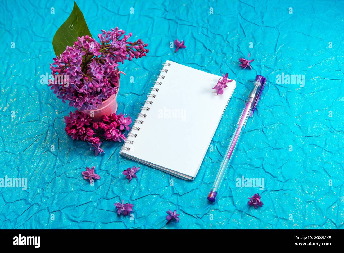 Blank notebook, pen with purple ink, lilac flowers on vintage blue paper background. Stock Photo
