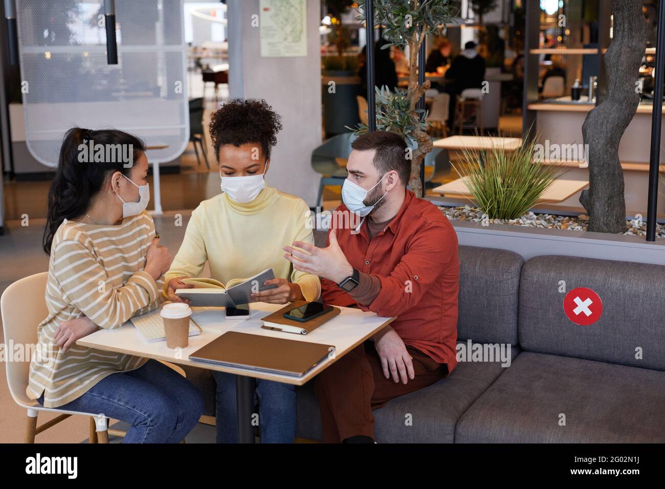 Diverse group of people wearing masks while working at table in cafe ...