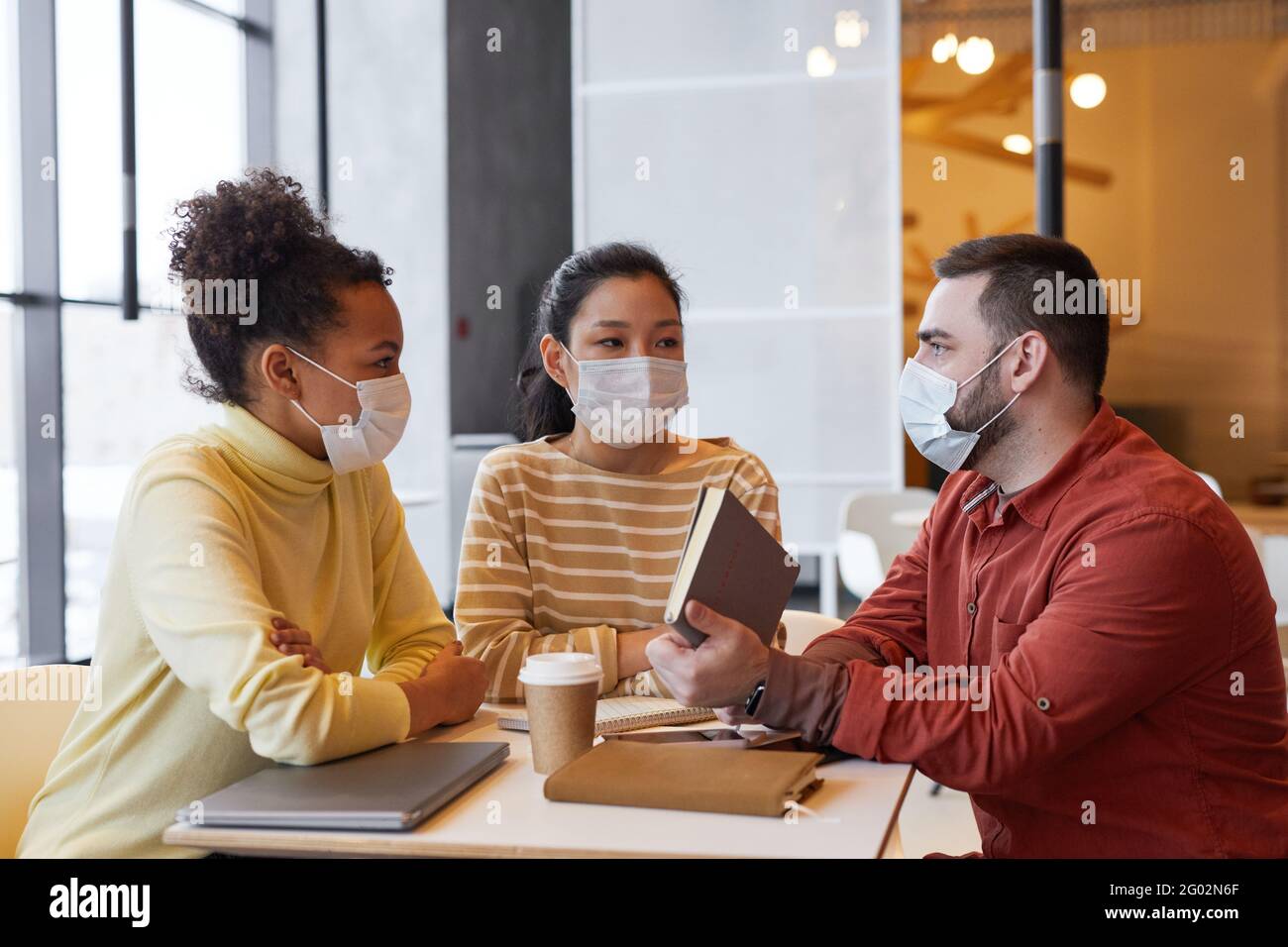Group of people wearing masks while working at table in cafe together ...