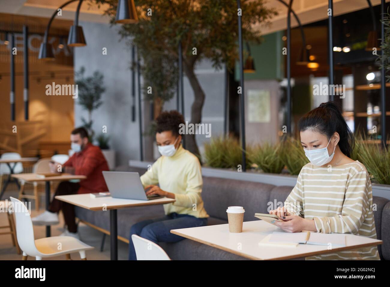 Group of people wearing masks while working at tables in cafe in row ...