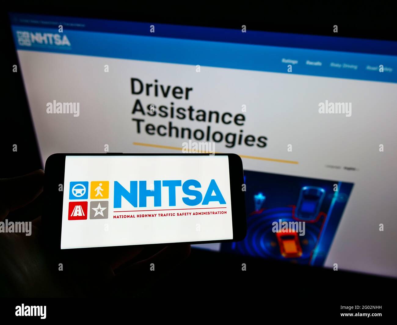 Person holding cellphone with logo of National Highway Traffic Safety Administration (NHTSA) on screen in front of web page. Focus on phone display. Stock Photo