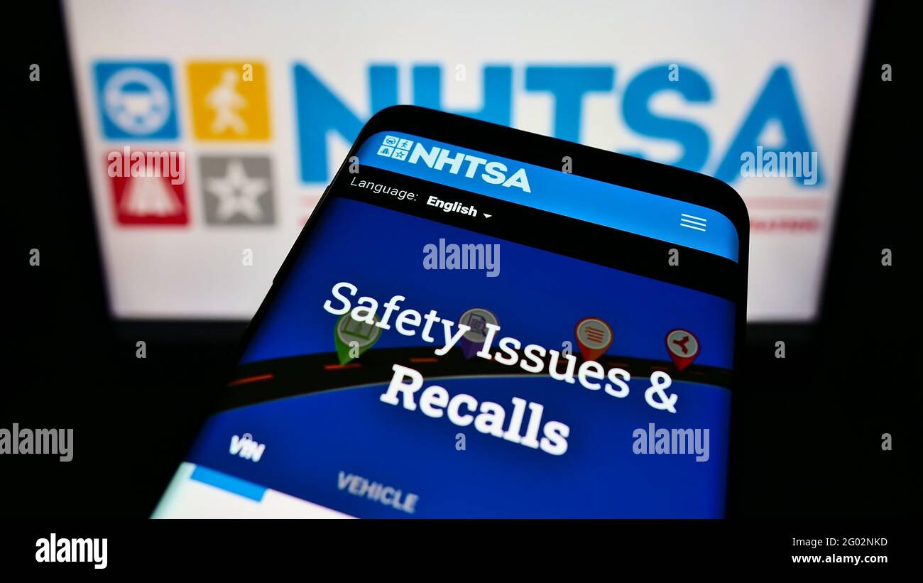 Mobile phone with website of National Highway Traffic Safety Administration (NHTSA) on screen in front of logo. Focus on top-left of phone display. Stock Photo
