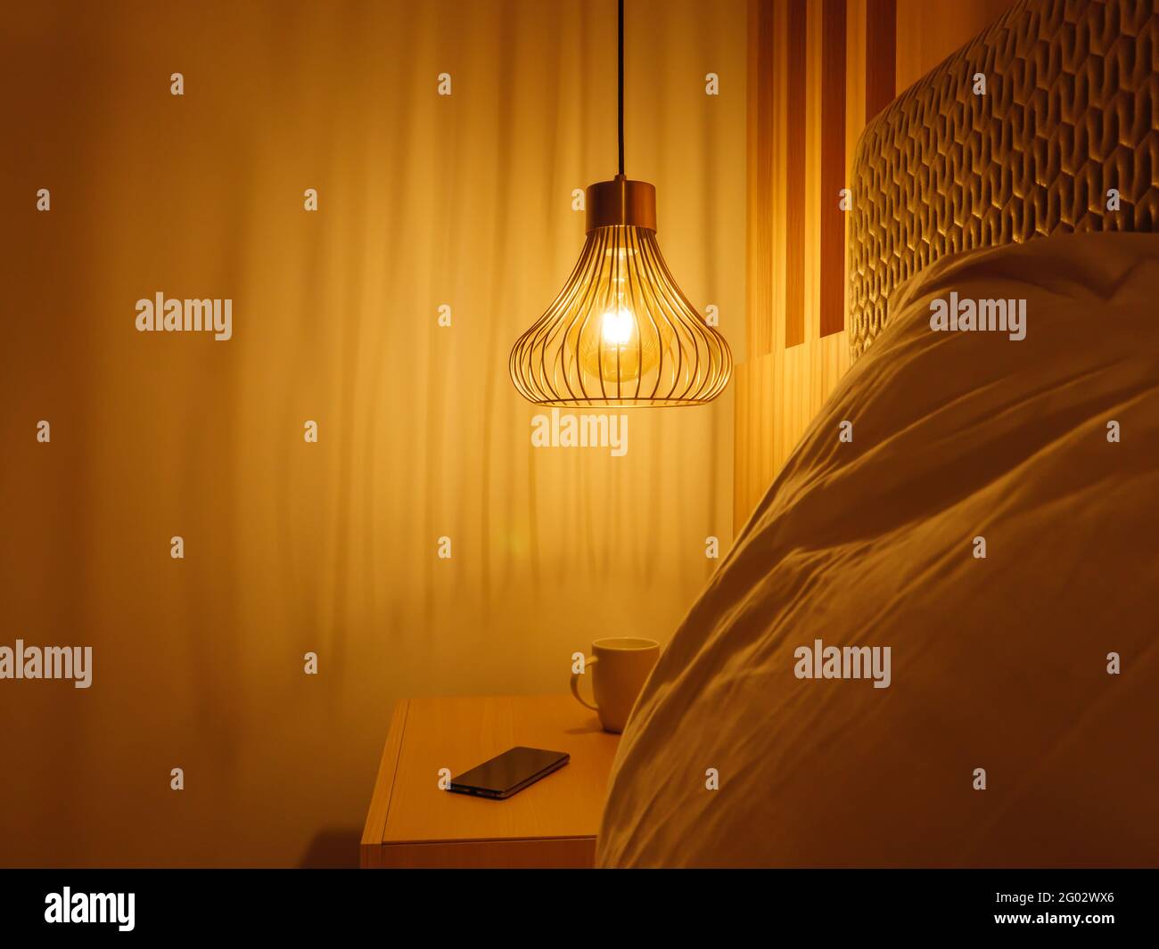 Metal lamp shade with yellow light above the bedside cabinet with