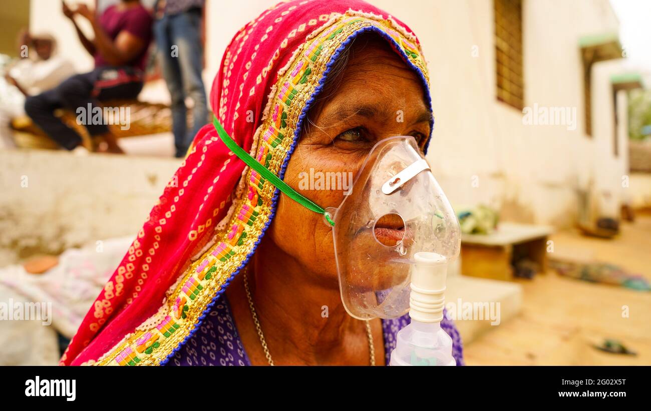 20 May 2021- Reengus, Sikar, India. Old Indian woman infected with Covid 19 disease. Patient inhaling oxygen wearing mask with liquid Oxygen flow. Stock Photo