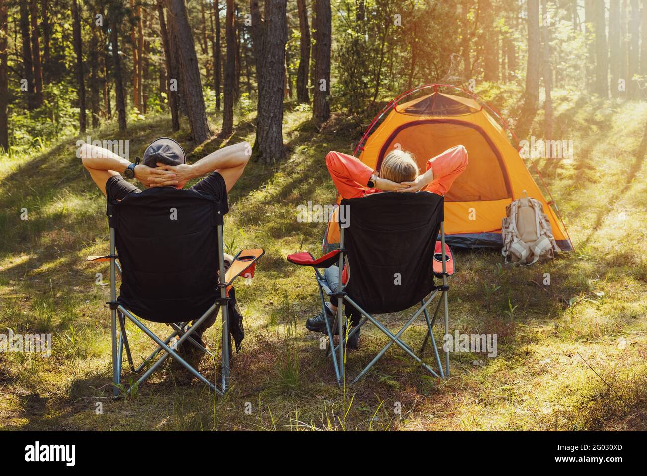 people relaxing in camping chairs at forest campsite and enjoying the nature Stock Photo