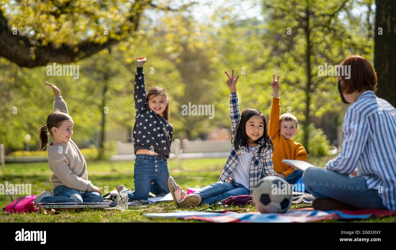 Small children with teacher outdoors in city park, learning group education and art concept. Stock Photo