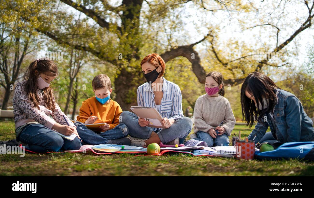 Teacher with small children sitting outdoors in city park, learning group education and coronavirus concept. Stock Photo