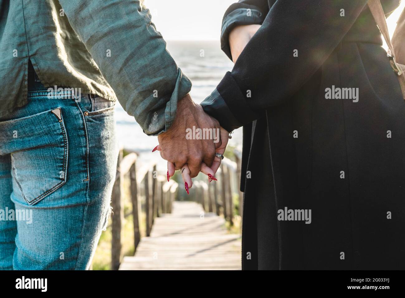 Closeup of young couple holding hands walking down on wooden stair towards the beach - Hipster couple, holding hands, in love enjoying romantic evenin Stock Photo