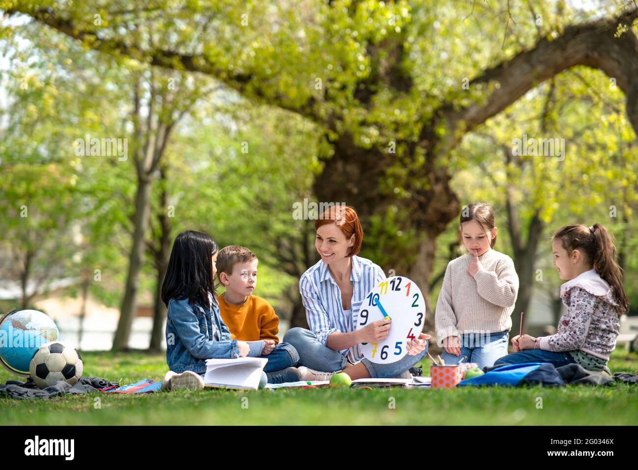 Teacher with small children sitting outdoors in city park, learning group education concept. Stock Photo