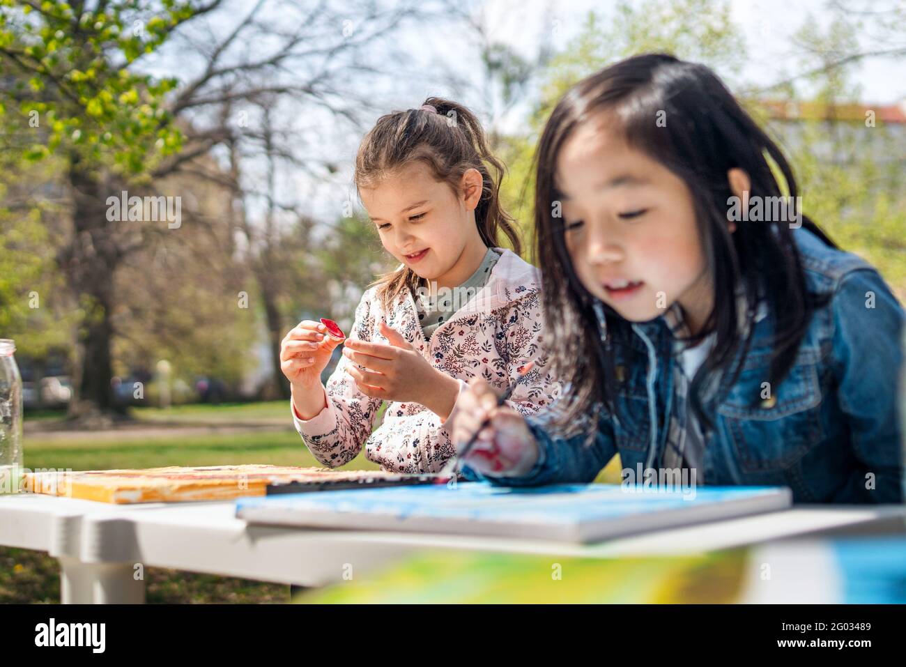 Small children painting pictures outdoors in city park, learning group education concept. Stock Photo