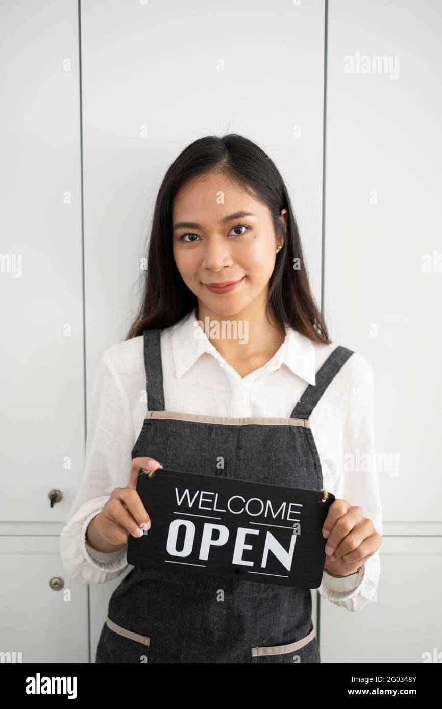 Portrait of waitress in apron holding open sign board while standing in coffee shop. Stock Photo