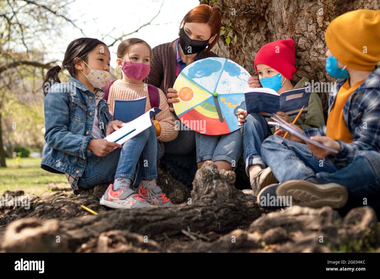 Teacher with small children sitting outdoors in city park, learning group education and coronavirus concept. Stock Photo