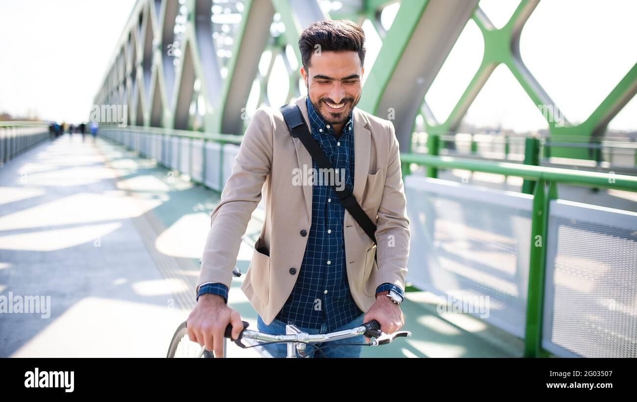 Young business man commuter with bicycle going to work outdoors in city, walking on bridge. Stock Photo