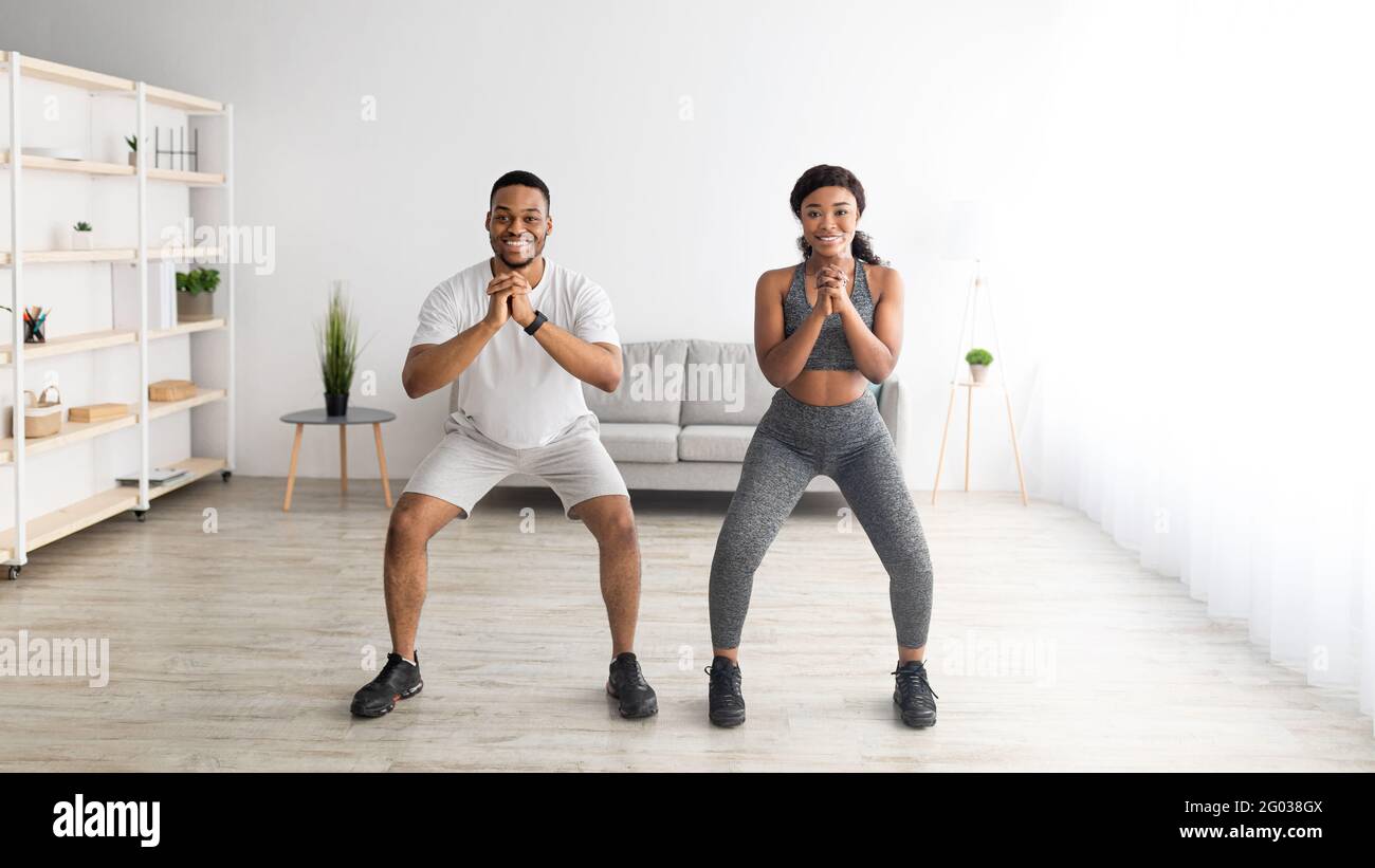 Domestic strength workout. Motivated black lady and her male partner doing squats together at home banner design Stock Photo Alamy