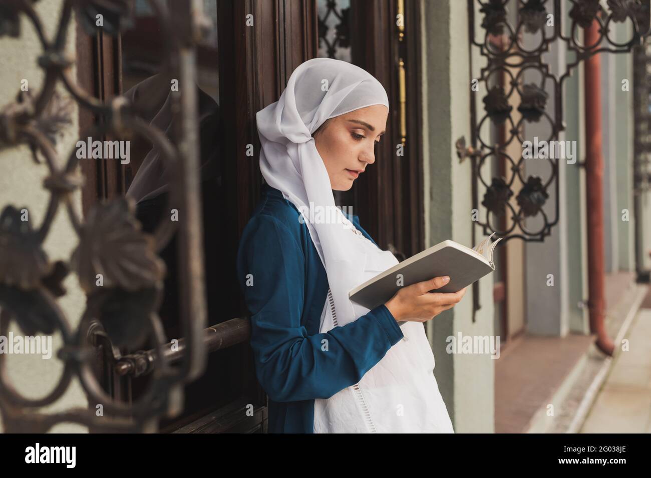 Portrait of young muslim woman wearing hijab reading book outdoors ...